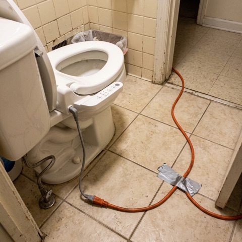 An electric bidet seat with an extension cord taped across the floor
